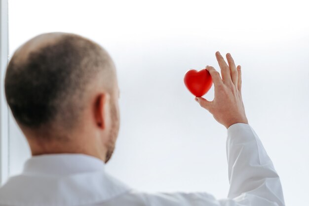 Retrovisore. il medico guarda il piccolo cuore rosso nelle sue mani. il concetto di tutela della salute.