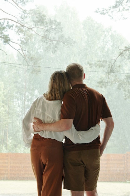 Vista posteriore di una giovane coppia sognante che si abbraccia e gode della vista dalla finestra