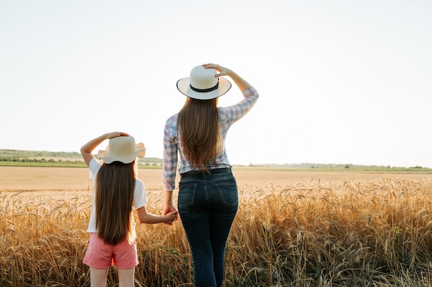 Rear view of family farmer woman and child with hat on golden wheat field at sunset