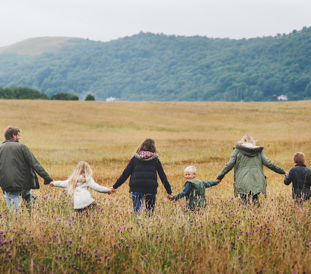 Foto vista posteriore della famiglia che si tiene per mano camminando in un campo