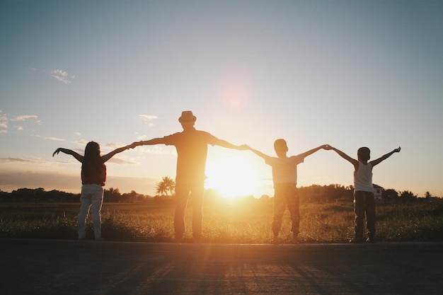 Photo rear view of family with holding hands while arms outstretched against sunset