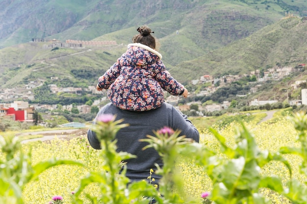 Rear view of father carrying daughter on shoulders in field