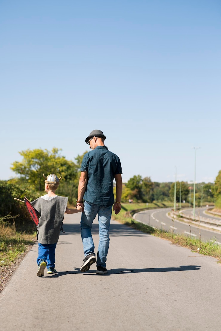 फोटो rear view of father and son walking on road against clear sky
