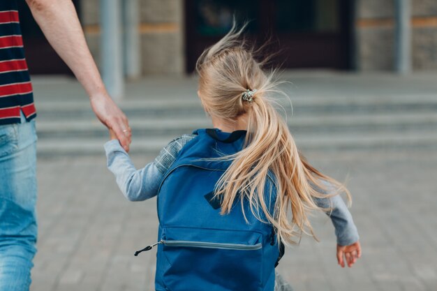 Rear view of father walking back to school with his daughter carrying backpack