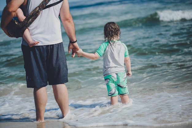 Photo rear view of father with children standing on shore at beach