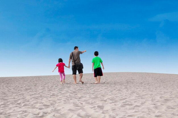 Rear view of father with children walking at beach against sky