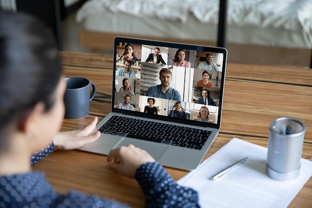 Rear view of female employee talk speak on video call with\
diverse multiethnic coworkers from home office woman have webcam\
team online meeting or web virtual group conference with\
colleagues