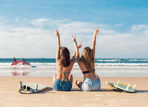 Photo rear view of female friends sitting at beach against sky