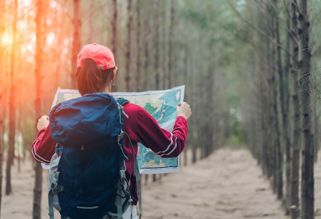 森に立って地図を読んでいる女性ハイカーの後ろの景色