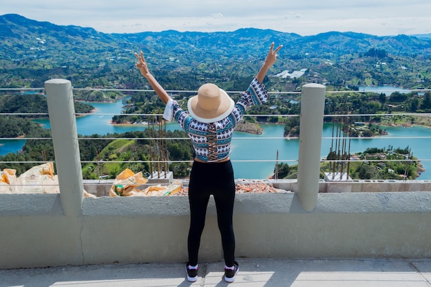 Rear view of female tourist raising hands at the edge of the Penol stone in Guatape Colombia