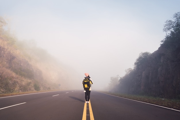 Rear view of a female traveler walking in the middle of the paved road.