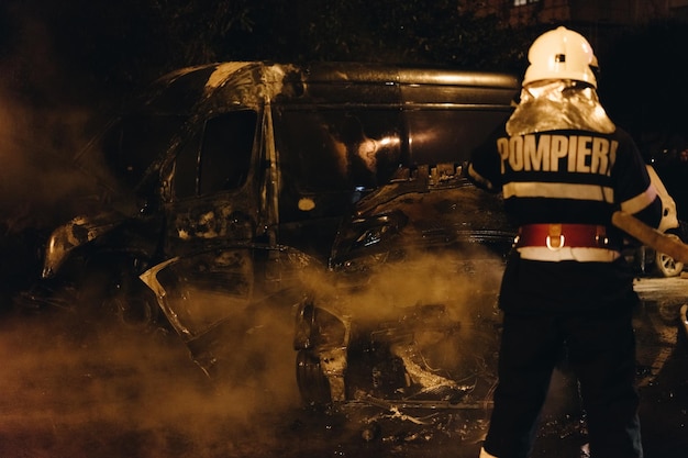 Photo rear view of firefighter standing by damaged car at night
