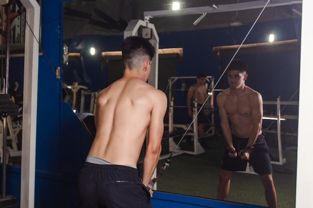 Rear view of a fitness guy training chest with the pulley at the gym.