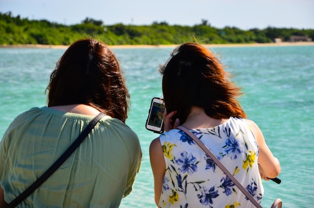 Photo rear view of friends looking at smart phone by sea