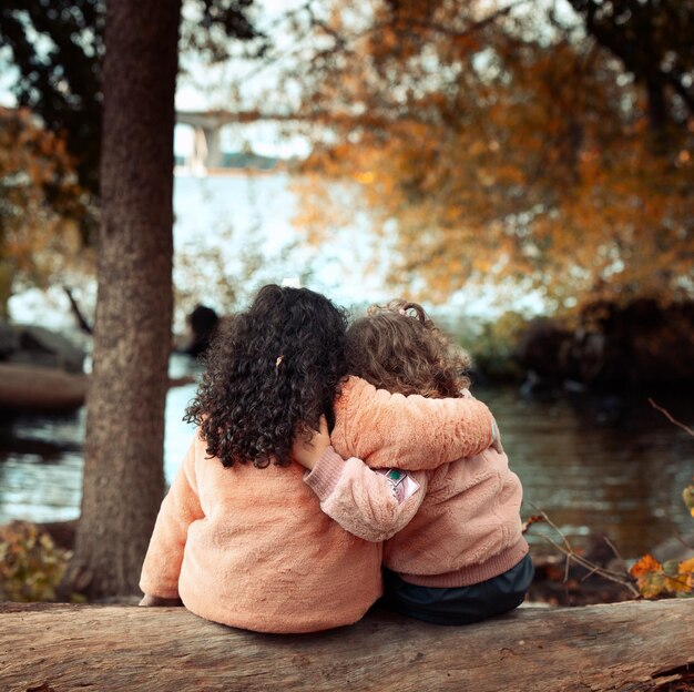 Rear view of friends sitting on log at autumn