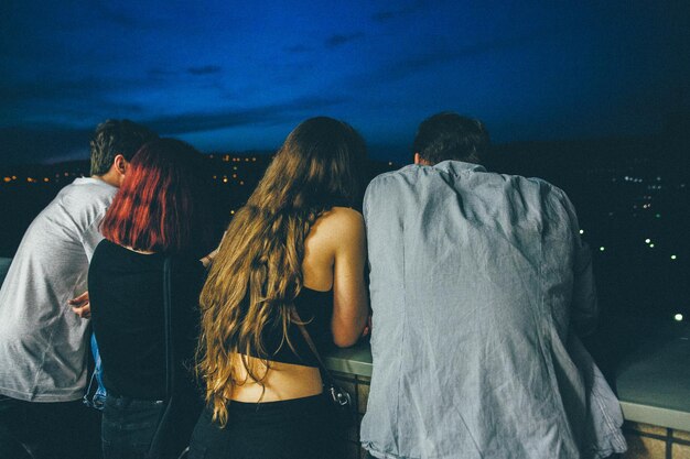 Rear view of friends standing against sky at dusk