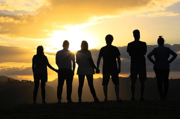 Foto vista posteriore di amici in piedi sul campo contro il cielo durante il tramonto