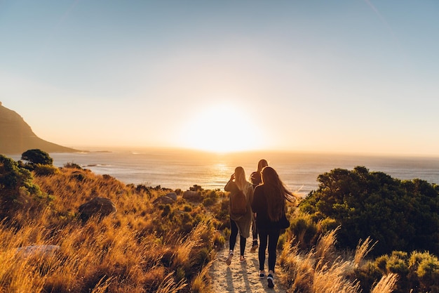 Rear view of friends walking at beach against clear sky during sunset