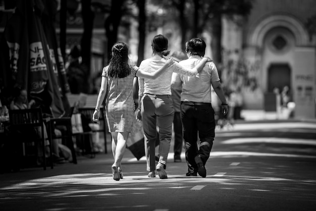 rear view of friends with arms around walking on street in city