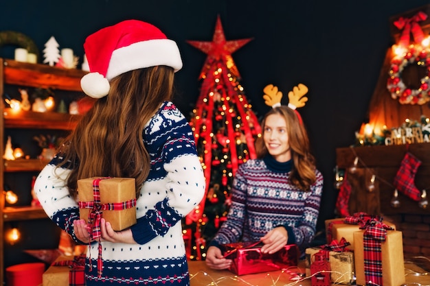 Rear view from the back of a cheerful mom and her cute daughter girl exchanging gifts.