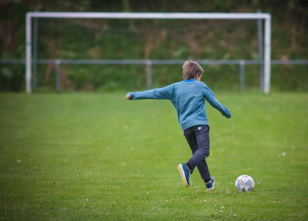 Photo rear view full length of boy playing soccer on field