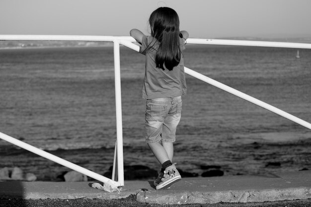 海に向かってレールに立っている女の子の全長の後ろの景色