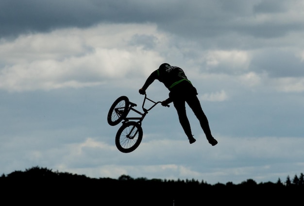 Rear view full length of man doing stunt with bicycle against sky