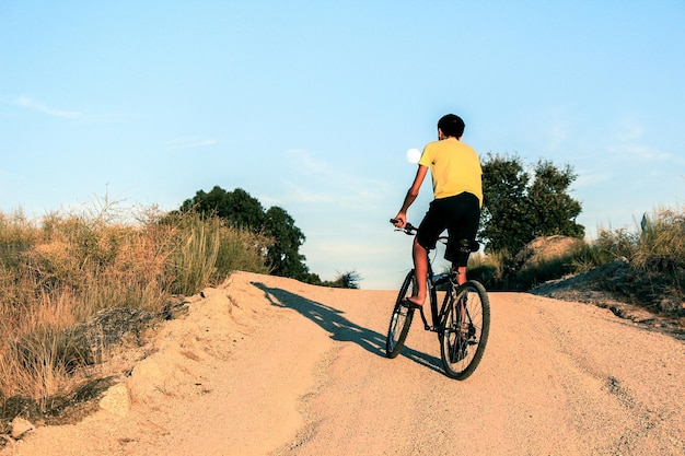 空の向こうの道路で自転車に乗っている男の全長の後ろの景色