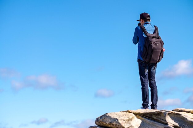 Rear view full length of man standing on rock against blue sky