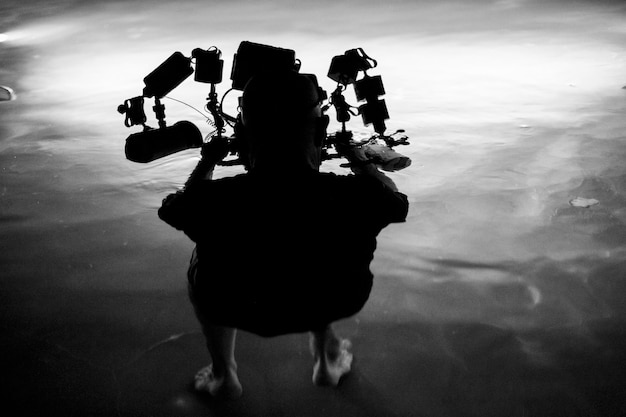 Foto vista posteriore a tutta lunghezza di un uomo con apparecchiature di illuminazione in mare di notte