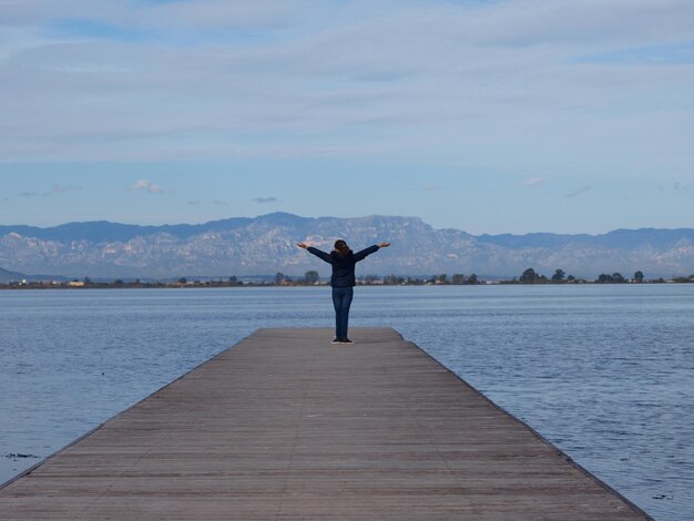 Rear view full length of woman with arms outstretched on pier amidst sea