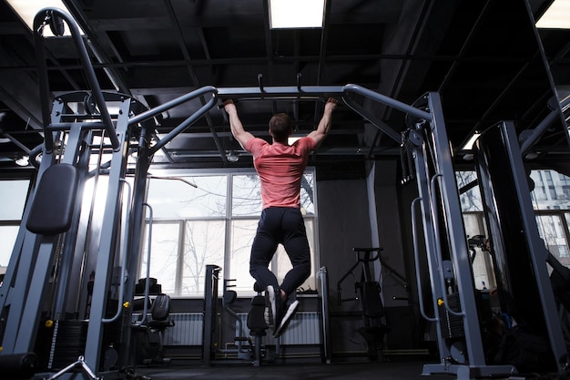 Rear view fulllength shot of an athletic muscular man doing pullups in crossover gym machine