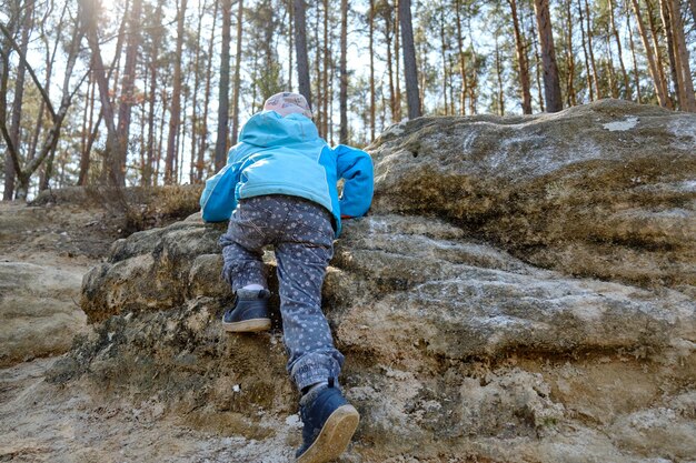 Foto vista posteriore di una ragazza che si arrampica su una formazione rocciosa nella foresta