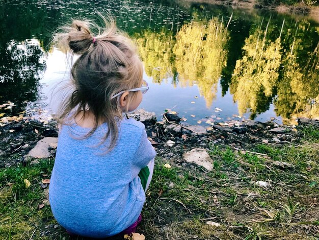 Photo rear view of girl crouching by lake with reflection