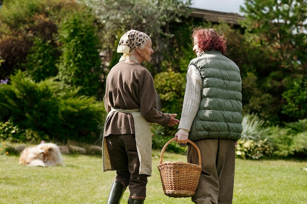 Rear view of girl and her grandmother chatting while moving down green lawn