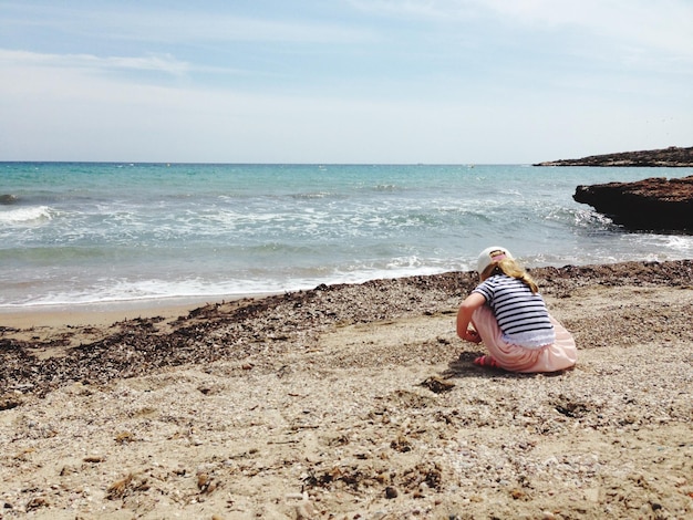 Foto vista posteriore di una ragazza che gioca sulla riva sulla spiaggia contro il cielo