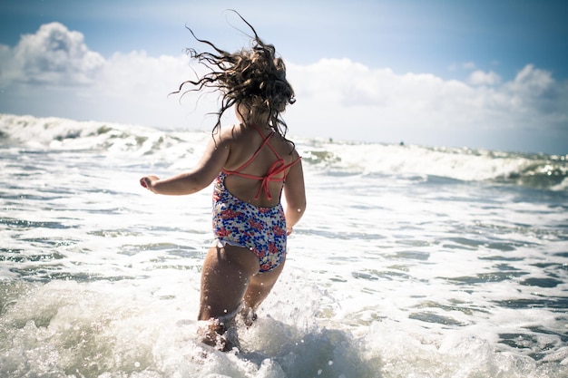 rear view of girl running in water against sky during sunny day
