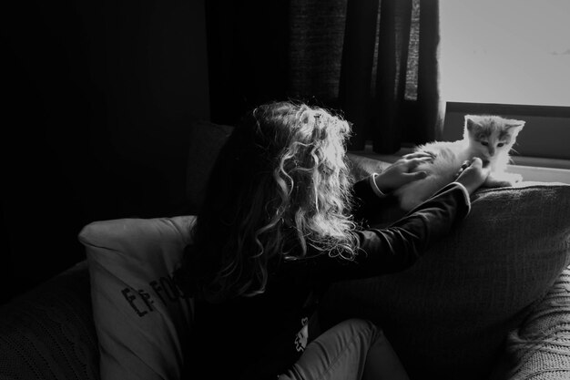 Photo rear view of girl on sofa with kitten at home