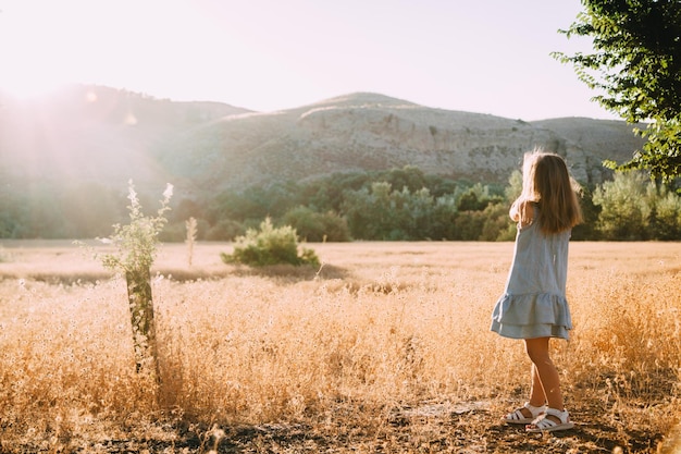 Foto vista posteriore di una ragazza in piedi su un campo erboso contro la montagna