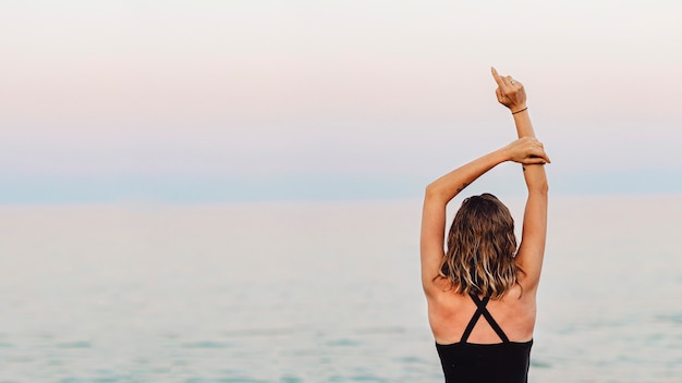 Rear view of a girl stretching her arms in the air at the beach