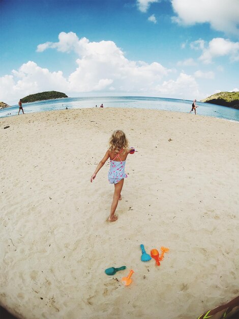 Rear view of girl walking at beach against sky