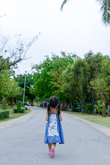 Rear view of girl walking on road against clear sky in park
