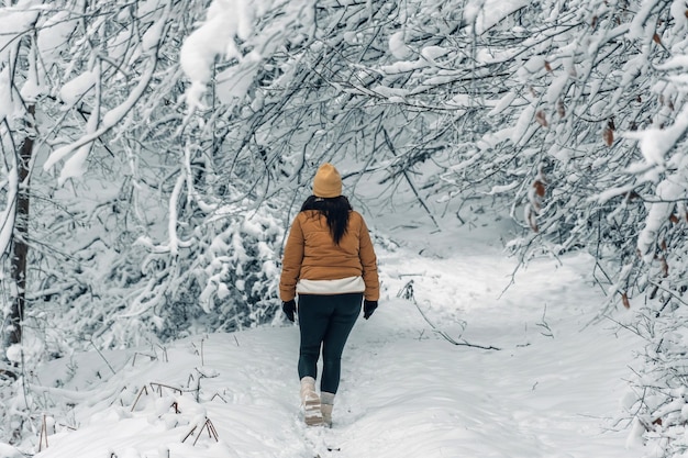 森の雪の道を歩く冬の服を着た女の子の後ろの景色