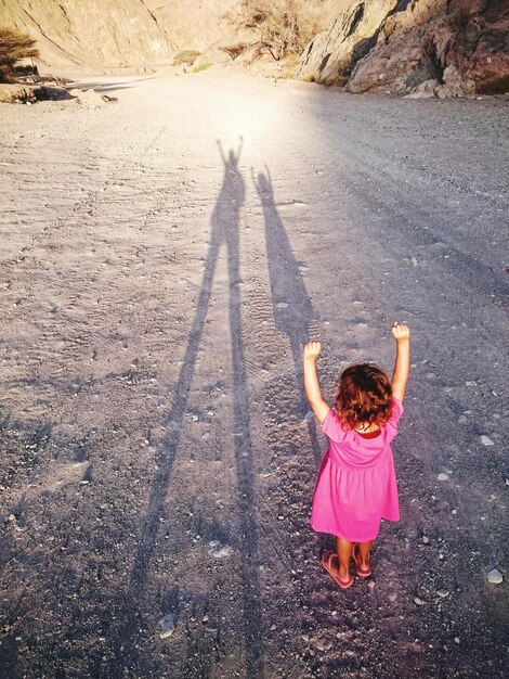 Foto vista posteriore di una ragazza con le braccia alzate in piedi di fronte all'ombra sul campo