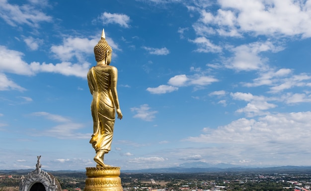 Rear view of the golden standing Buddha statue in the traditional Thai style located in the viewpoint on the high mountain