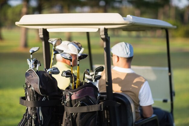 Rear view of golfer friends sitting in golf buggy