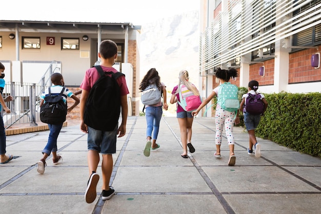 Rear view of group of diverse students with backpacks running at elementary school