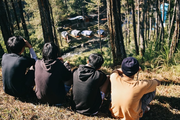 Rear view gtop viewroup of male friends sitting on grass and enjoying view from top hill