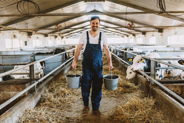 Вид сзади красивого кавказского фермера в целом держа ведра в руках с кормом для животных. Стабильный интерьер.