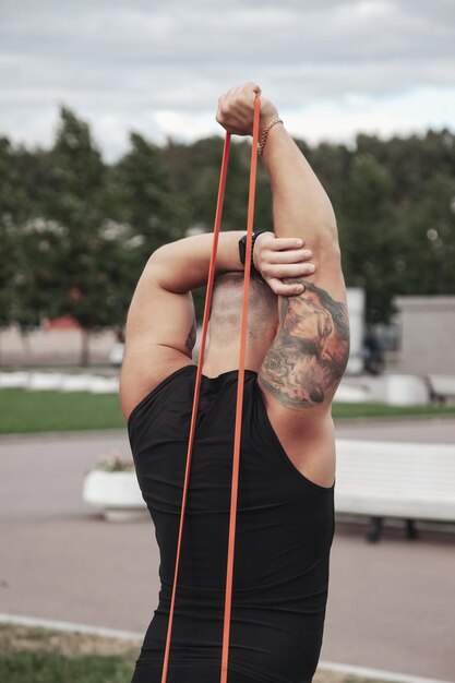 Rear view handsome man sportsman doing lunge workout with resistance band outdoors in urban park Fitness healthy lifestyle concept